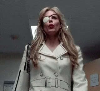 A Woman With A Bandage On Her Eye Is Wearing A White Trench Coat And Sunglasses . GIF