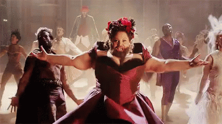 A Woman With A Beard In A Red Dress Is Dancing In Front Of A Group Of People . GIF