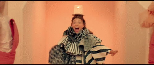 A Woman With A Box On Her Head Is Wearing A Striped Outfit GIF