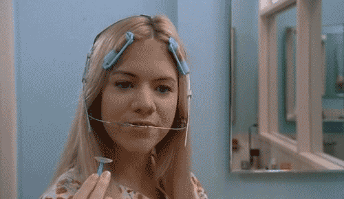 A Woman With A Brace On Her Head Holds A Razor In Front Of A Mirror GIF