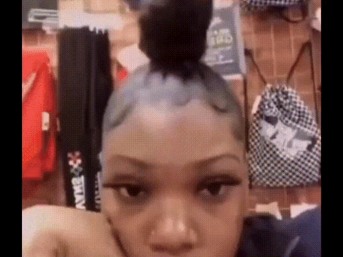 A Woman With A Bun On Her Head Is Sitting In Front Of A Wall With Clothes Hanging On It . GIF