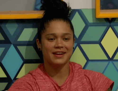 A Woman With A Bun On Her Head Is Smiling In Front Of A Wall With Geometric Shapes GIF