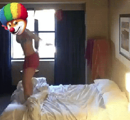 A Woman With A Clown Mask On Her Head Jumps On A Bed GIF