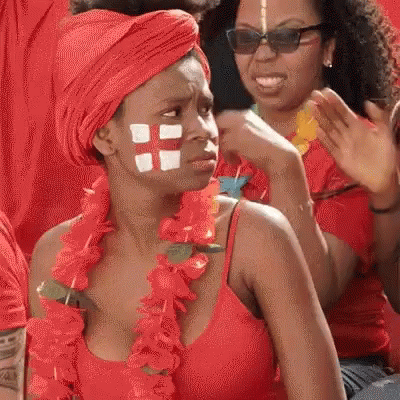 A Woman With A Cross Painted On Her Face Is Wearing A Red Top And A Red Turban . GIF