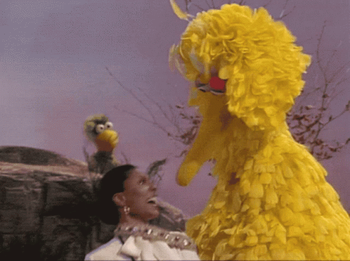 A Woman With A Crown On Her Head Stands Next To A Big Bird GIF