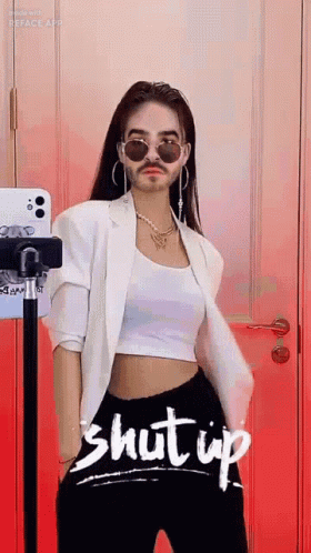 A Woman With A Fake Mustache And Sunglasses Is Standing In Front Of A Red Wall . GIF