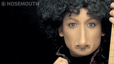 A Woman With A Fake Nose Is Holding A Guitar And Making A Face GIF