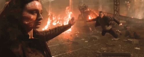 A Woman With A Flame On Her Face Is Standing In Front Of A Burning Building GIF