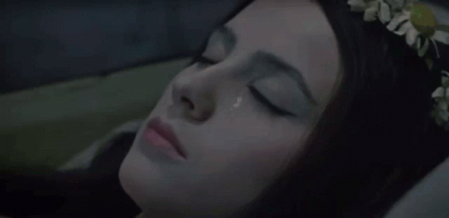 A Woman With A Flower Crown On Her Head Is Laying In Bed With Her Eyes Closed GIF