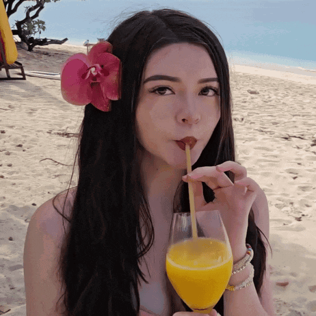 A Woman With A Flower In Her Hair Drinking From A Straw GIF