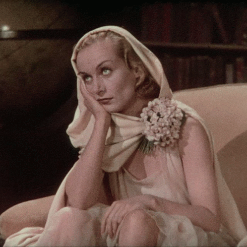 A Woman With A Flower In Her Hair Is Sitting In A Chair With Her Hand On Her Face GIF