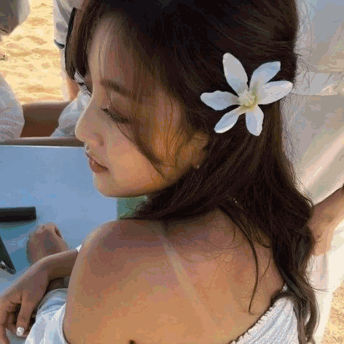 A Woman With A Flower In Her Hair Is Sitting On The Beach GIF