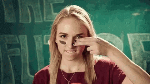 A Woman With A Football On Her Face Is Smiling And Covering Her Nose With Her Hand . GIF