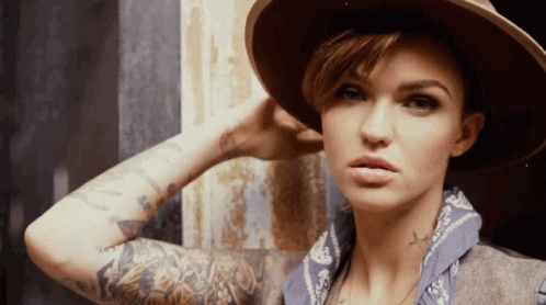 A Woman With A Hat And A Bandana Has A Cross Tattoo On Her Arm GIF