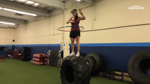 A Woman With A Hula Hoop On Top Of A Tire In A Gym With The Words Awesome Behind Her GIF