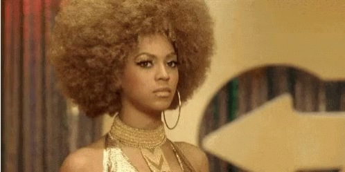 A Woman With A Large Afro Is Wearing A Gold Dress And Hoop Earrings . GIF