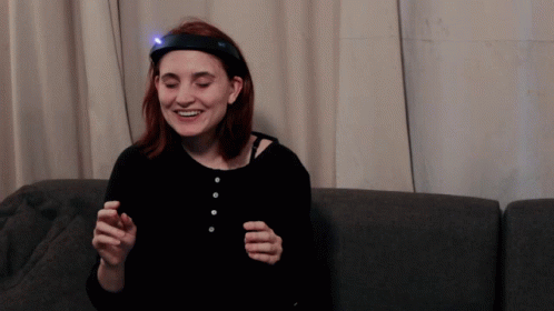 A Woman With A Light On Her Head Is Smiling GIF