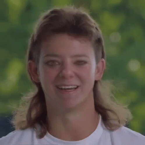 A Woman With A Mullet And A White Shirt Smiles GIF