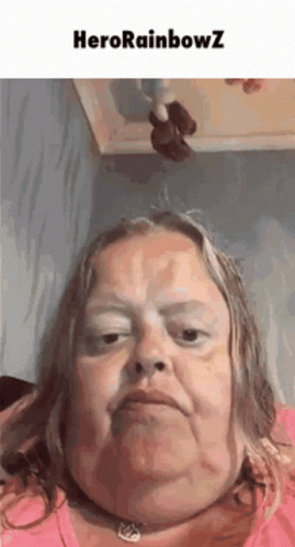 A Woman With A Necklace Around Her Neck Is Making A Funny Face With The Words Herorainbowz Above Her . GIF