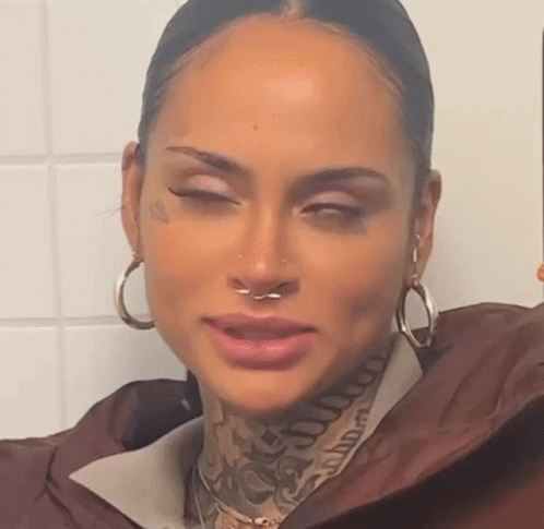 a woman with a nose ring and tattoos on her face is taking a selfie .