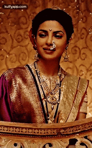 A Woman With A Nose Ring Is Wearing A Purple And Gold Sari And Jewelry . GIF