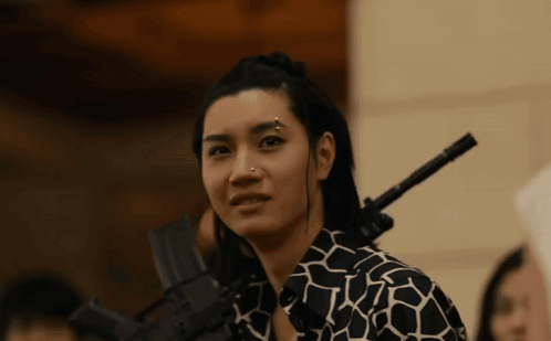 A Woman With A Piercing On Her Nose Is Holding A Gun On Her Shoulder GIF