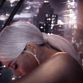 A Woman With A Ponytail And Earrings Looks Down At Something GIF
