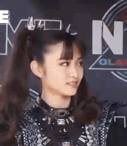 A Woman With A Ponytail Is Standing In Front Of A Sign That Says ' N ' On It . GIF