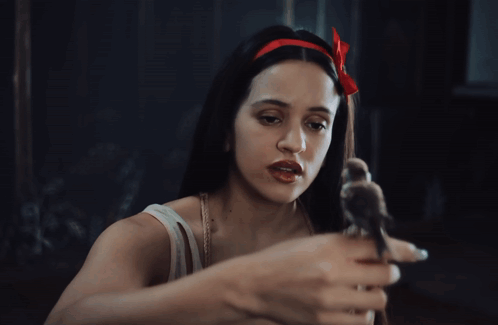 A Woman With A Red Bow In Her Hair Holds A Small Bird In Her Hand GIF