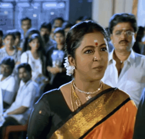 A Woman With A Red Dot On Her Forehead Stands In A Crowd Of People GIF