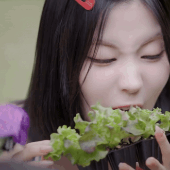 A Woman With A Red Hair Clip Is Eating Lettuce From A Container GIF