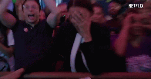 A Woman With A Ring On Her Finger Is Covering Her Mouth In A Crowd Of People With Netflix Written On The Bottom GIF