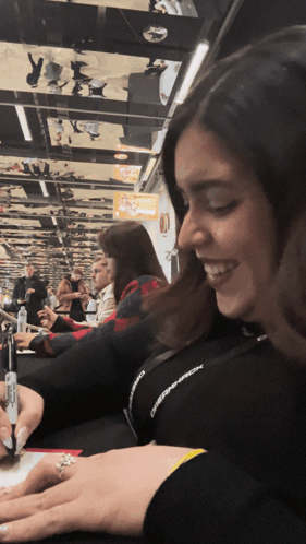A Woman With A Ring On Her Finger Is Smiling In Front Of A Crowd Of People GIF
