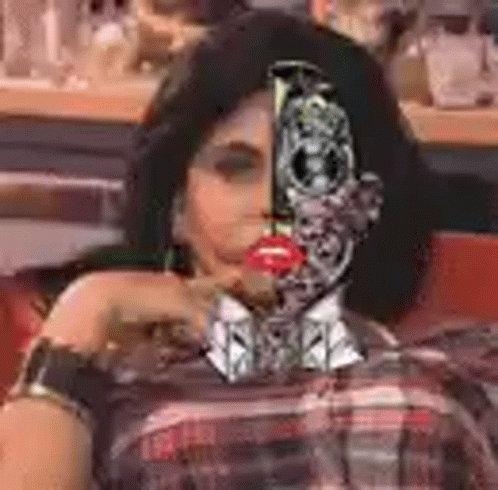A Woman With A Robot Face On Her Face Is Sitting In A Chair . GIF