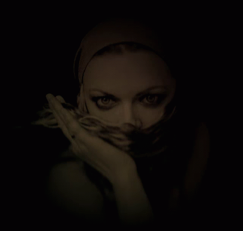 A Woman With A Scarf Around Her Face Looks At The Camera GIF