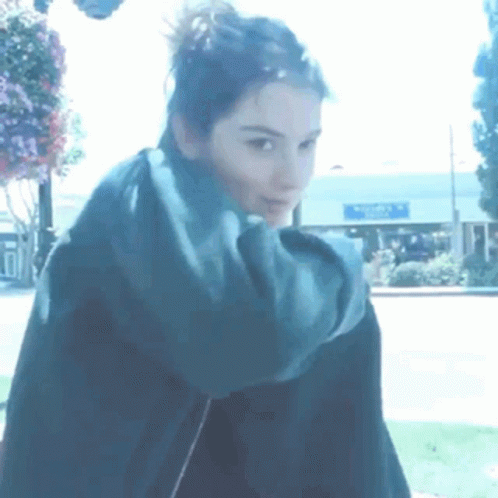 A Woman With A Scarf Around Her Neck Is Standing In Front Of A Building That Says Walmart GIF