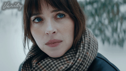 A Woman With A Scarf Around Her Neck Looks At The Camera With The Word Verity Below Her GIF