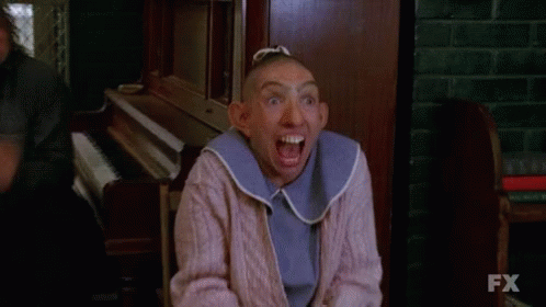 A Woman With A Shaved Head And A Bib On Her Neck Is Making A Funny Face . GIF