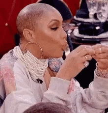 A Woman With A Shaved Head Is Sitting At A Table Eating A Sandwich . GIF