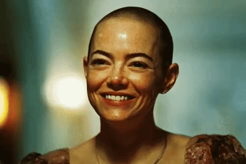 a woman with a shaved head is smiling in a dark room .