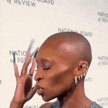 a woman with a shaved head is standing in front of a national board of review banner