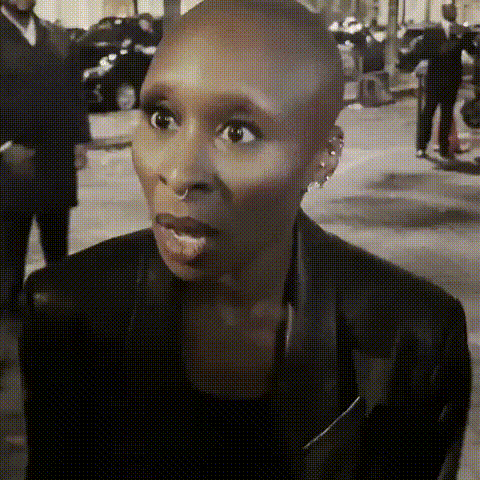 A Woman With A Shaved Head Is Wearing A Black Jacket And Earrings . GIF