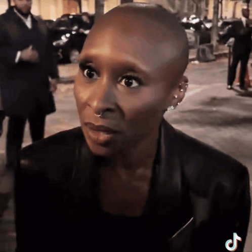 A Woman With A Shaved Head Is Wearing A Black Jacket And Has A Tiktok Logo On Her Shoulder GIF