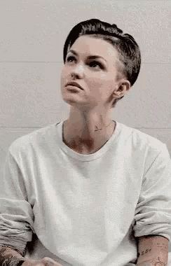 A Woman With A Shaved Head Is Wearing A White Shirt . GIF