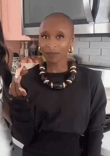 A Woman With A Shaved Head Wearing A Black Sweater And A Black Necklace GIF