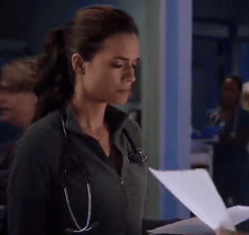 A Woman With A Stethoscope Around Her Neck Looks Down At A Piece Of Paper GIF