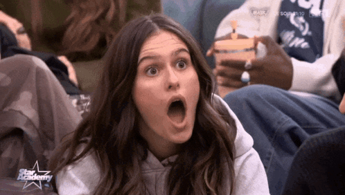 Surprised Woman Sitting In Front Of Star Academy Sign GIF