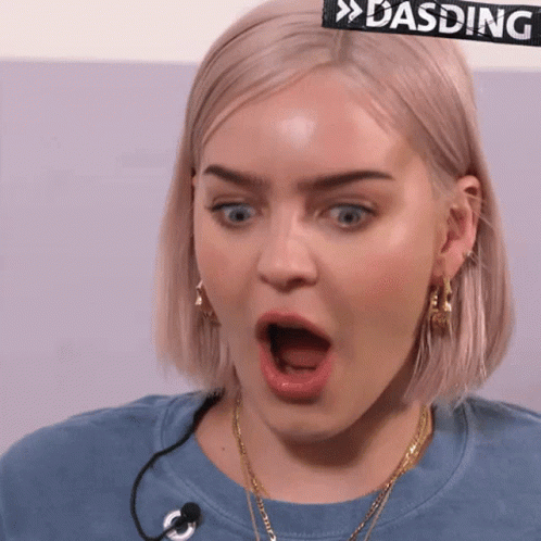 A Woman With A Surprised Look On Her Face Is Wearing A Blue Shirt With A Microphone . GIF