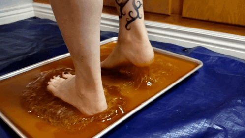 A Woman With A Tattoo On Her Ankle Is Standing On A Tray Of Liquid GIF
