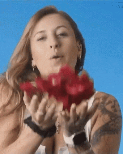 A Woman With A Tattoo On Her Arm Is Blowing Red Roses Into The Air GIF